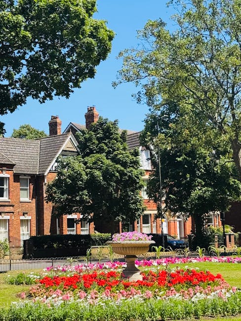 A neatly landscaped garden featuring a well-maintained, lush green lawn bordered by garden beds filled with a variety of flowering plants and ornamental foliage. The beds contain vibrant pink, purple,